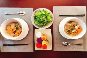 Two bowls of noodle soup with chopsticks and a bottle of sauce on a table.