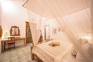 A bedroom with a canopy bed, a wooden desk, a mirror, and a door with a decorative frame. - Villa Papaya (Pecatu)