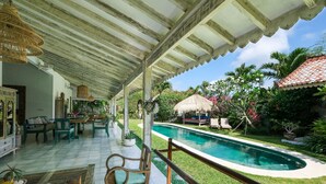 Eine überdachte Terrasse mit Pool, Gartenmöbeln und üppiger Bepflanzung.
