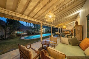 Un patio exterior techado con piscina, zona de estar y una estatua de Buda.