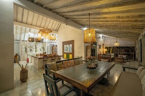 A spacious dining area with a long wooden table, multiple chairs, and hanging wicker lamps. - Villa Papaya (Pecatu)