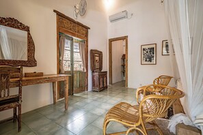 A room with a wooden table, wicker chairs, a mirror, and a door leading to another room. - Villa Papaya (Pecatu)