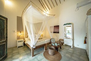 Un dormitorio con cama con dosel, mesita de noche, una silla, una cesta tejida y un espejo.