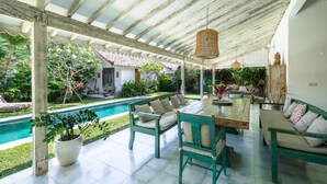 Eine Terrasse im Freien mit Pool, Holzmöbeln und einem überdachten Bereich mit Decke.