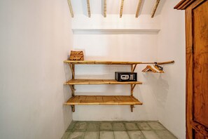 Un couloir étroit, avec une étagère en bois le long du mur, un petit tabouret rembourré et un porte-manteau muni de cintres.