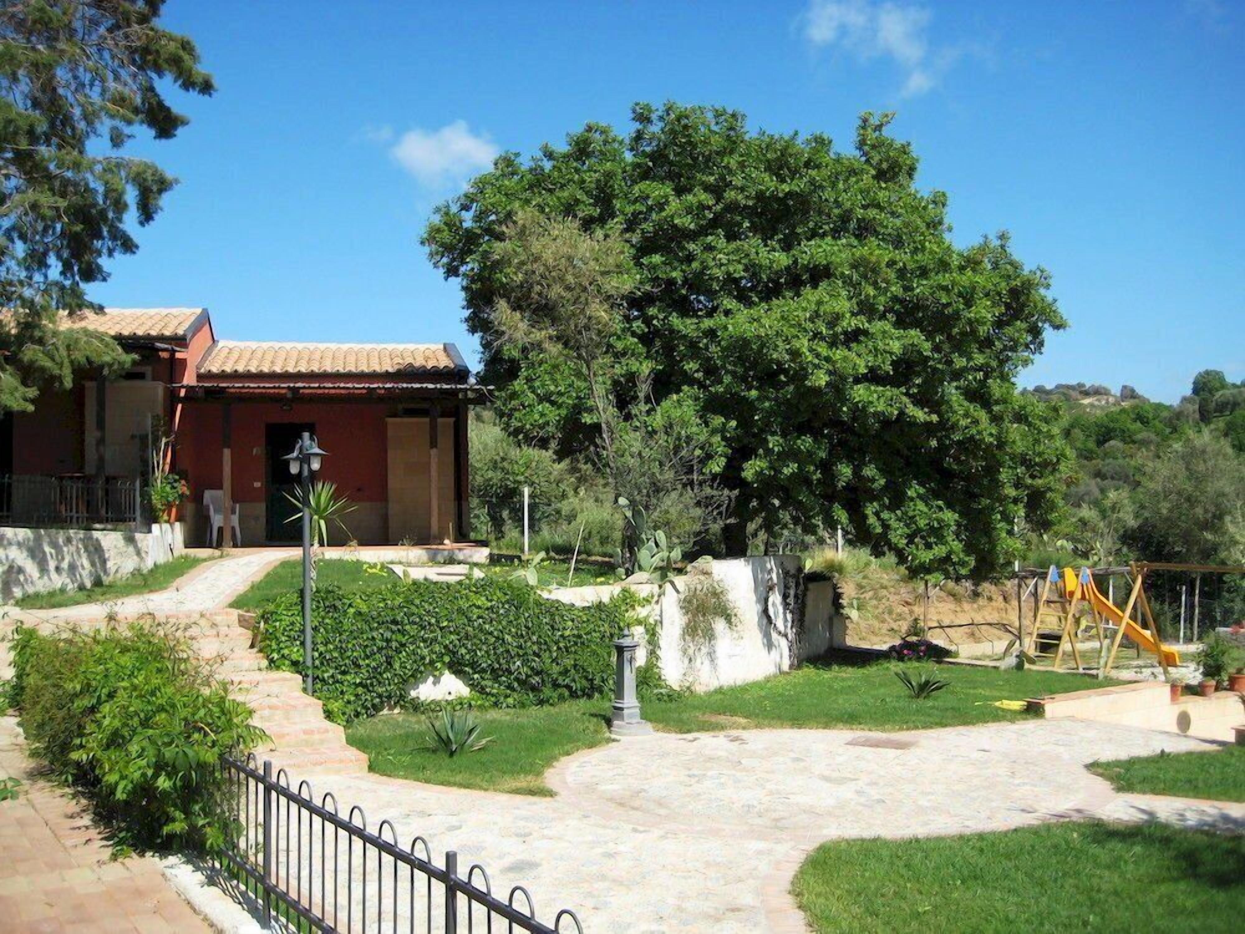 Una casa con techo de tejas, un camino empedrado y un jardín vallado.