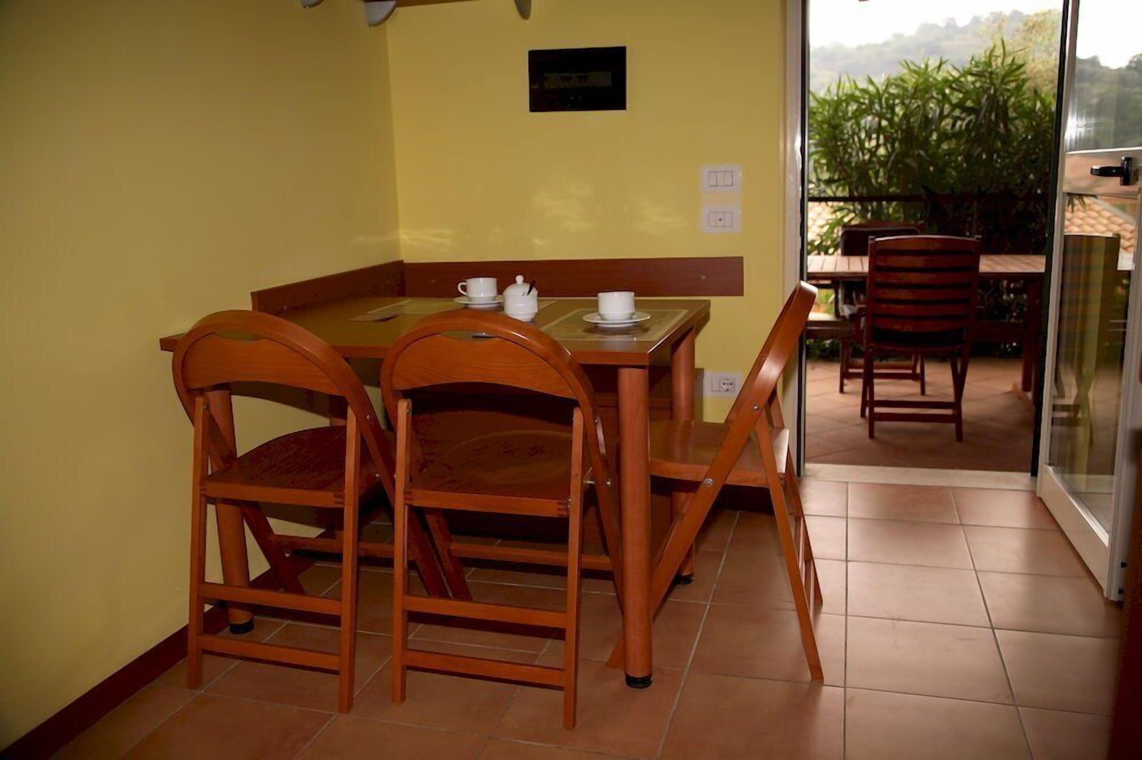 A dining area with a wooden table and chairs, a small white cabinet, and a view of the outdoors through a glass door.