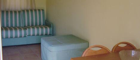 A dining area with a wooden table and chairs, a light-colored sofa with striped cushions, and a small ottoman.