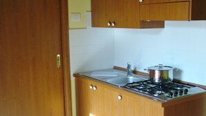 A compact kitchen with wooden cabinets, a stove, and a sink. - Residenza Mediterranea (Zambrone)