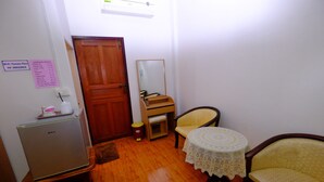 A compact room with a wooden door, a small table with a lace tablecloth, a yellow chair, and a refrigerator.
