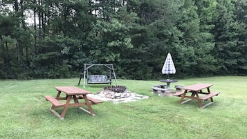 Un patio trasero con un parque infantil de madera, un brasero y dos mesas de picnic.