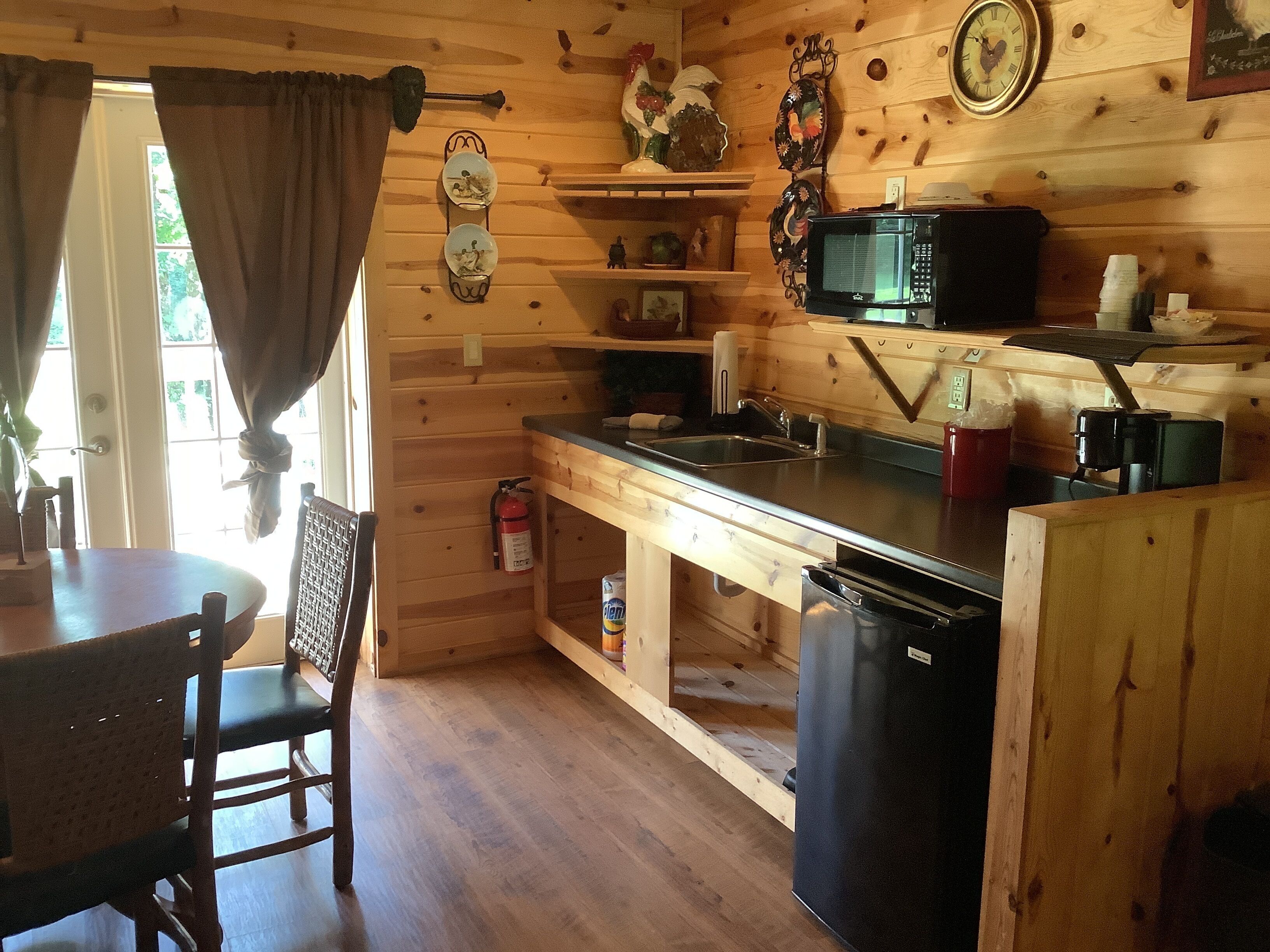 A wooden cabin kitchen with a sink, stove, and microwave. There is a dining table and chairs, and a fire extinguisher on the floor.