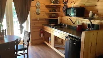 A wooden cabin kitchen with a sink, stove, and microwave. There is a dining table and chairs, and a fire extinguisher on the floor.