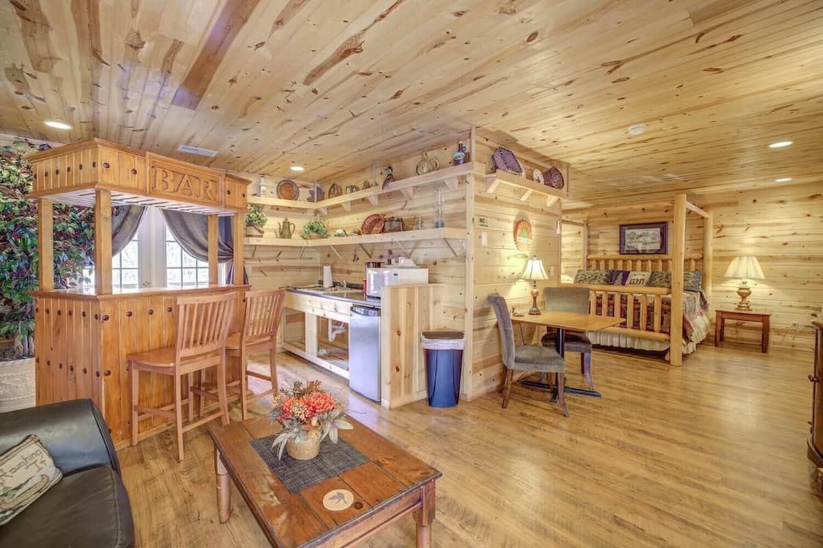 A cozy log cabin interior with a dining area, kitchen, and a small seating area with a bed.