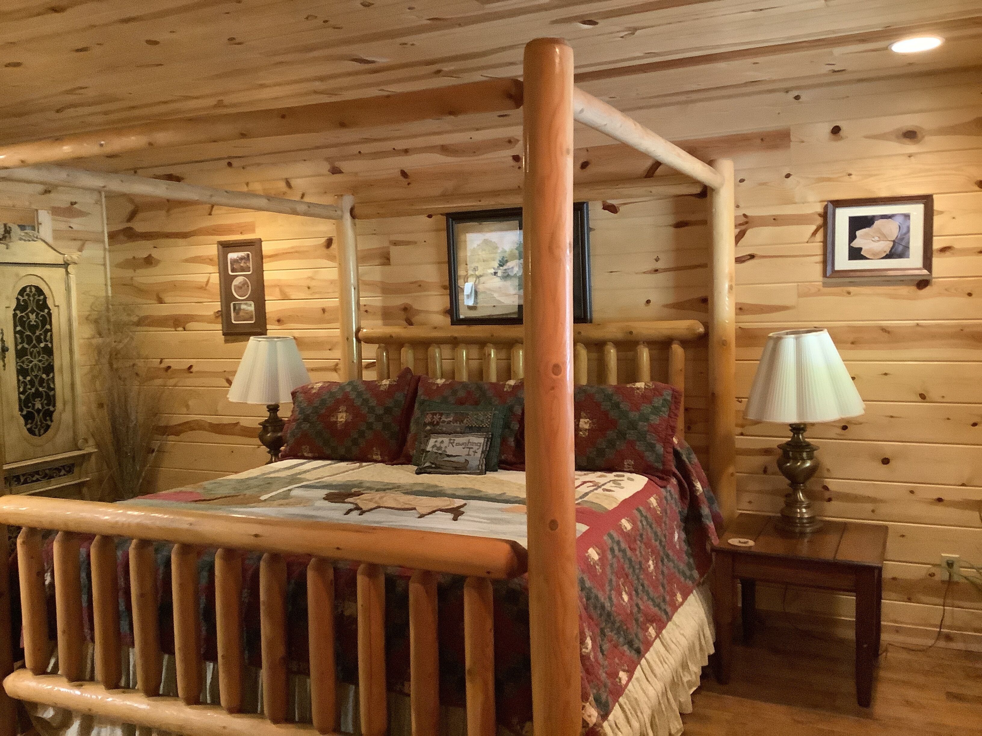 Une chambre à coucher dans un chalet en bois, avec un lit à baldaquin, deux lampes de chevet et un tableau encadré au mur.