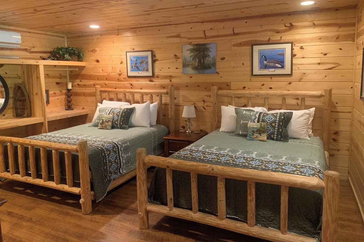A wooden cabin room with two beds, a mirror, and framed pictures on the walls.