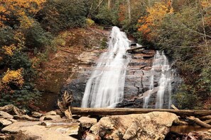 A waterfall cascading over rocks in a forested area with autumn foliage.