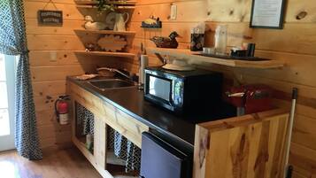Une petite cuisine aux murs en bois, avec un évier, un four à micro-ondes et un petit réfrigérateur. Un panneau est accroché au mur avec l’inscription : « Les pêcheurs sont les bienvenus ».