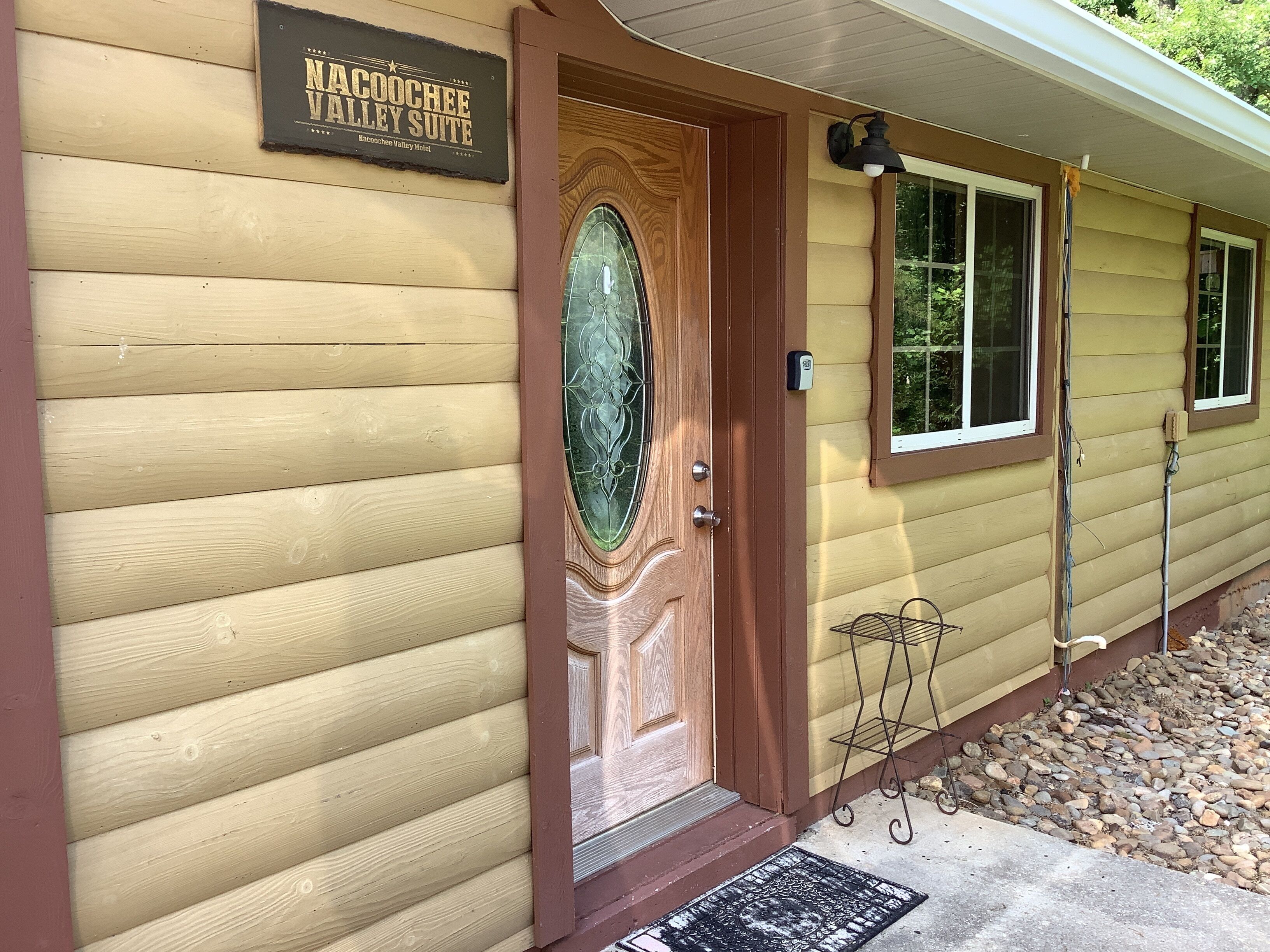 A wooden building with a sign reading "Nacoochee Valley Suite" and a door with a glass panel.