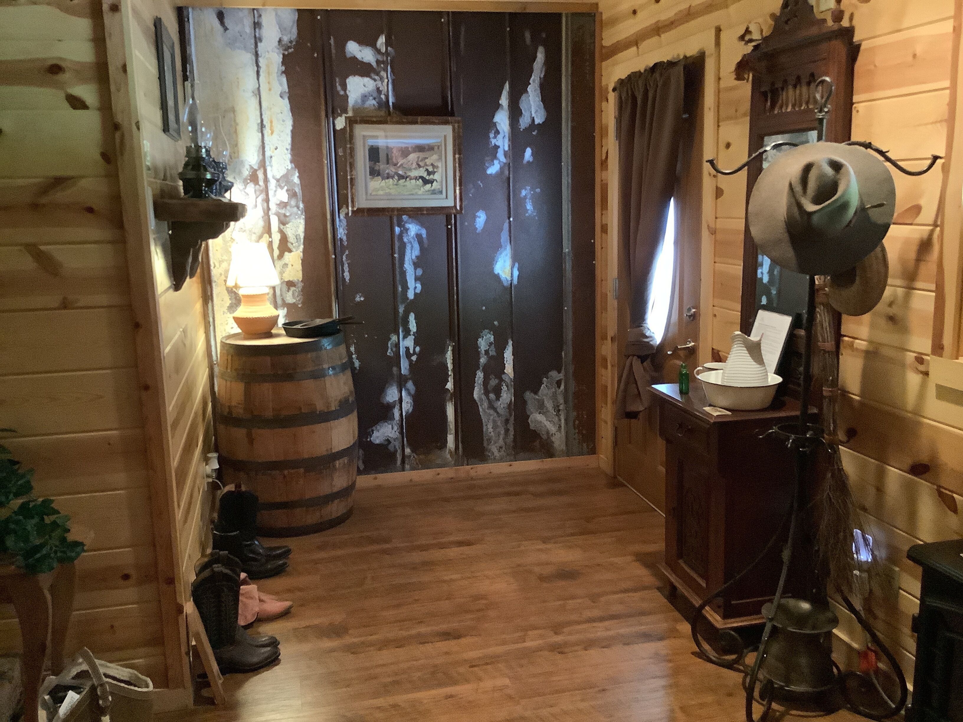 A wooden interior with a door, a lamp, a hat, and a barrel.