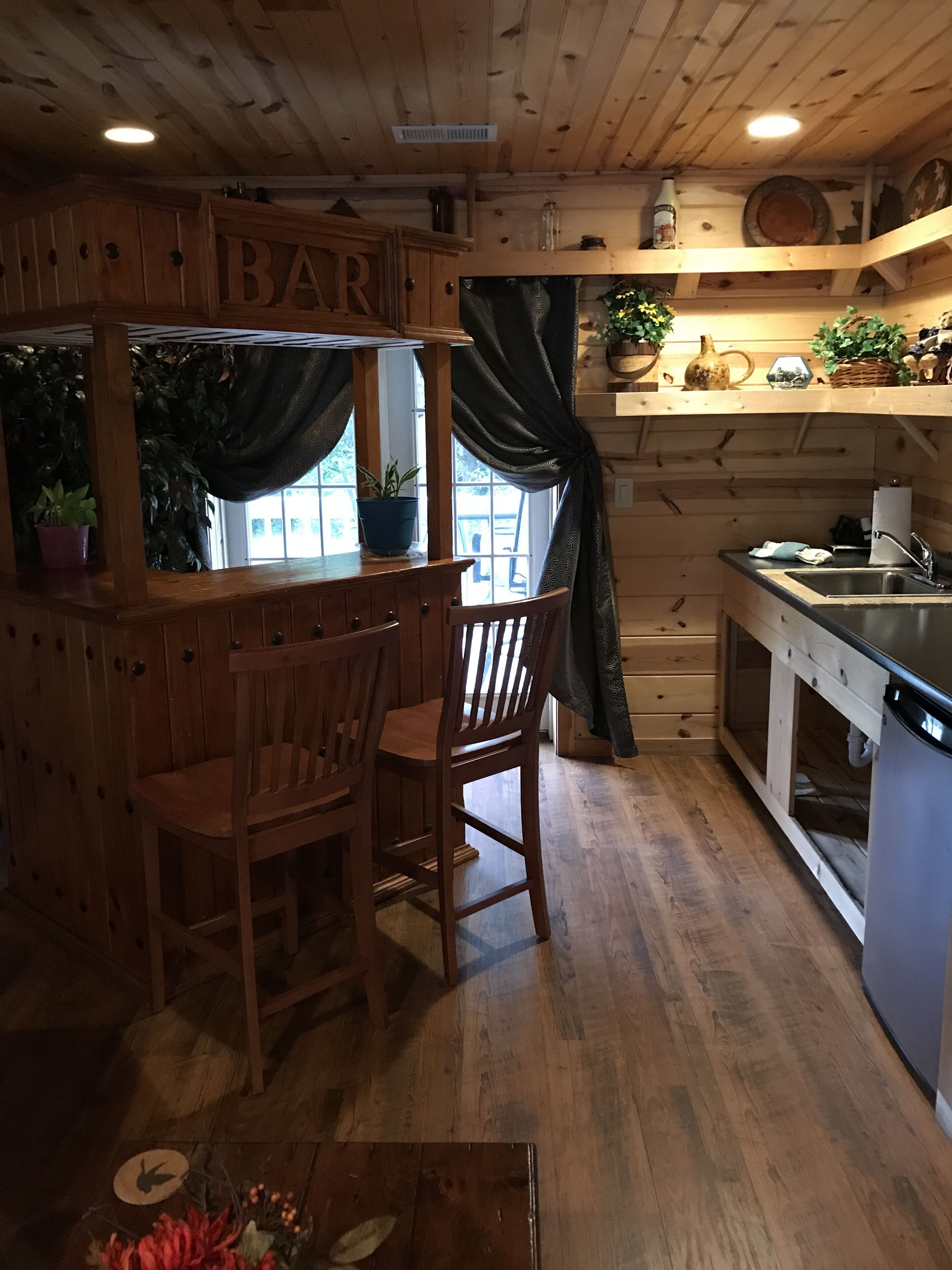 Un intérieur rustique en bois, avec un coin bar, des chaises en bois, un évier et des plantes en pot.