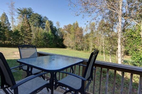 An outdoor deck with a table and chairs, surrounded by trees and a grassy area.