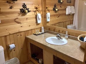 A wooden bathroom with a sink, mirror, towel rack, and a small shelf with toiletries.