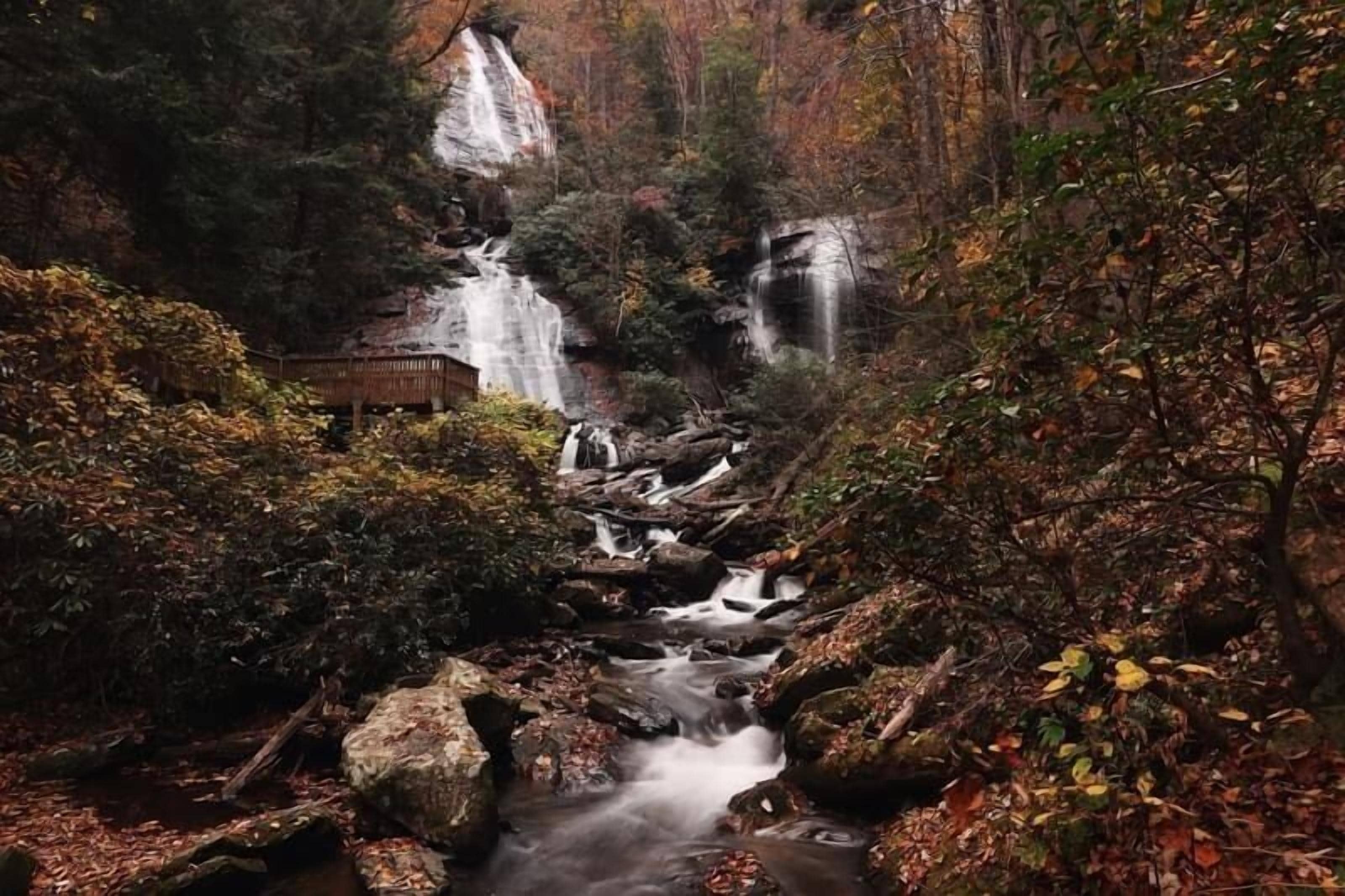 A waterfall cascading over rocks in a forested area with a wooden structure nearby.