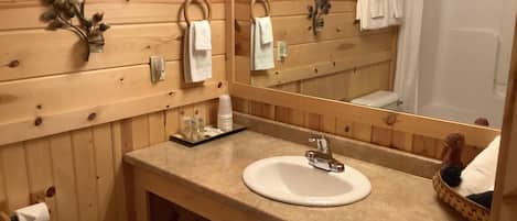 A wooden cabin bathroom with a sink, mirror, towel rack, and shower.