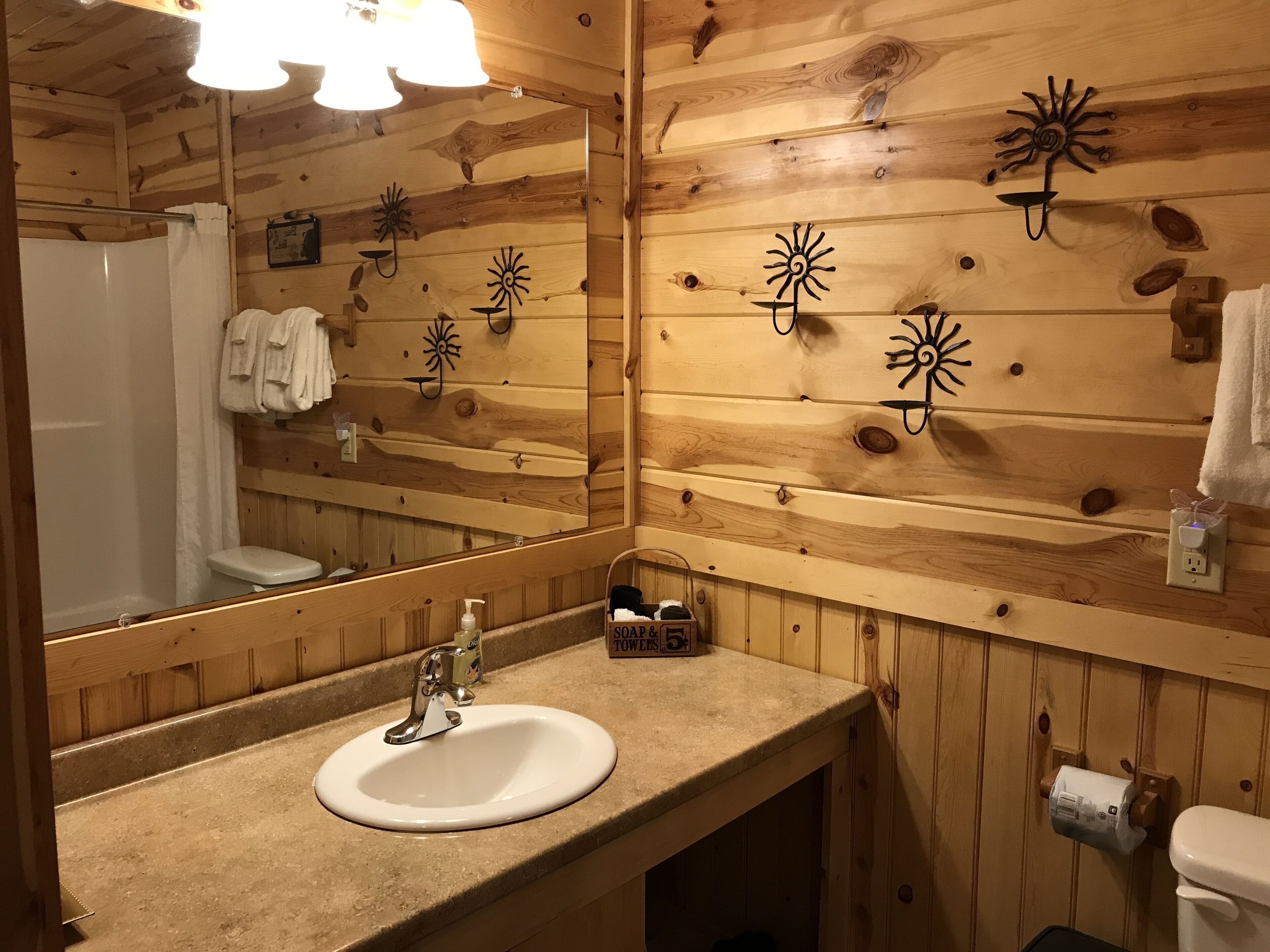 A wooden cabin bathroom with a sink, mirror, towel rack, and toilet.