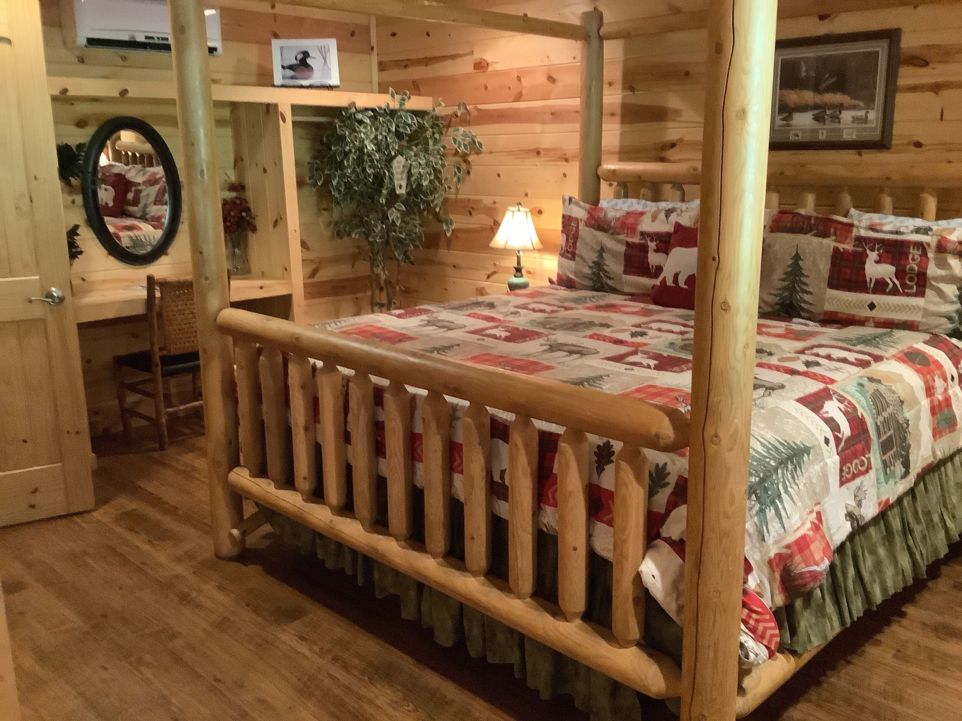 Ein zimmer im Blockhausstil mit einem hölzernen Himmelbett, einem kleinen Schreibtisch mit Stuhl, einem Spiegel und einem an der Wand befestigten Fernseher.