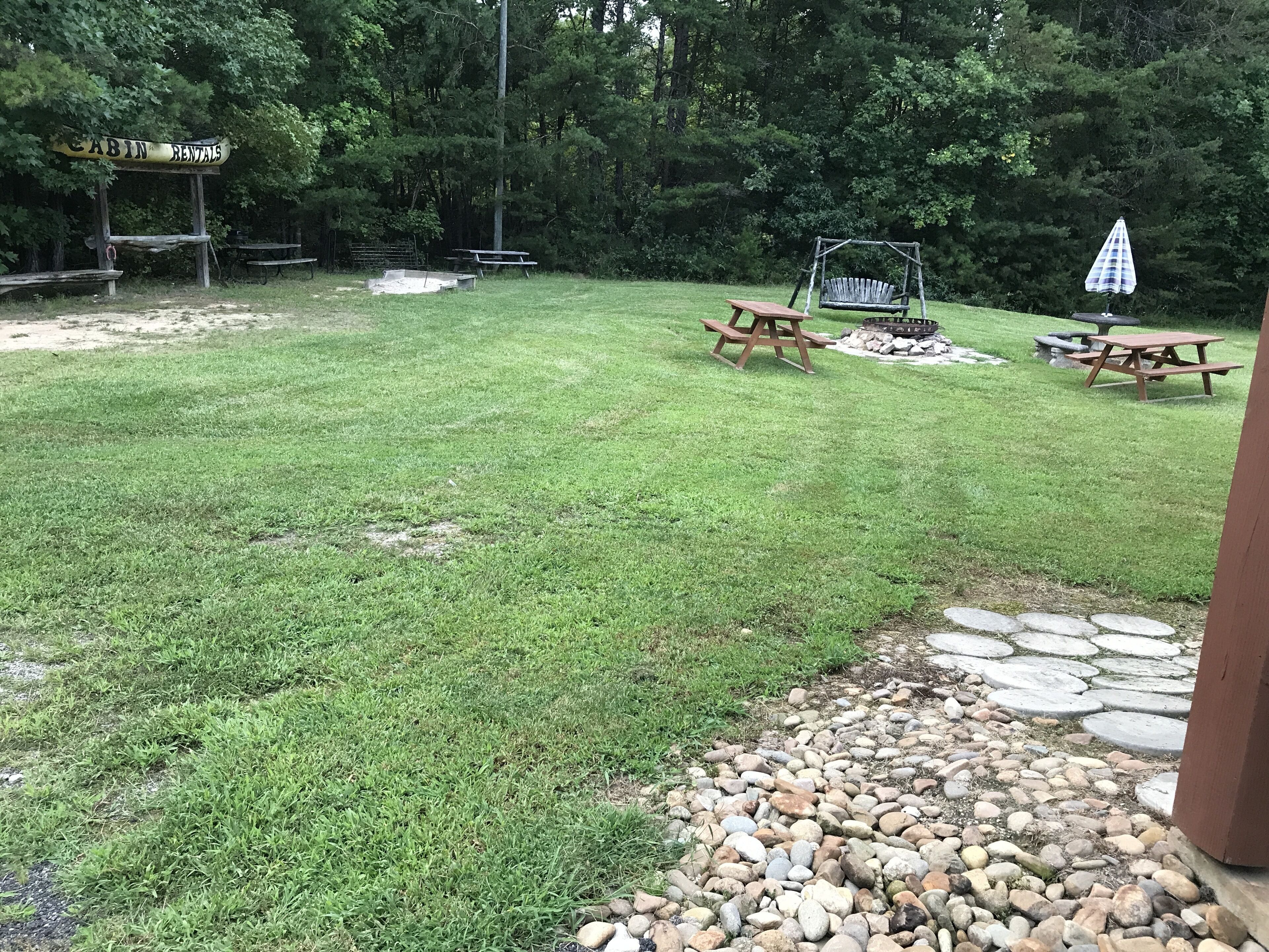 A grassy backyard with picnic tables, a swing set, and a fire pit.