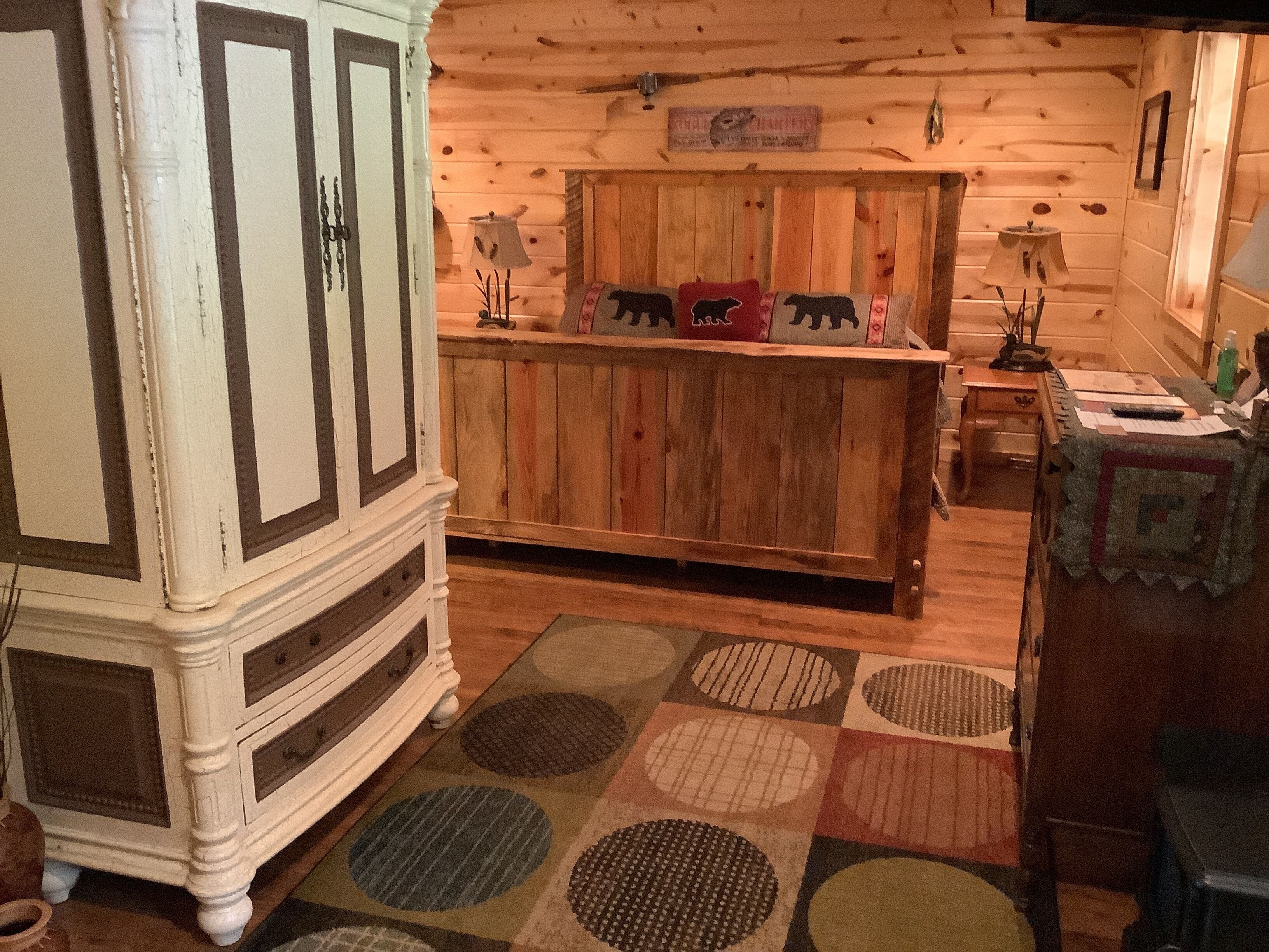 A rustic cabin interior with a wooden cabinet, a wooden counter with animal-themed decorations, and a patterned rug.