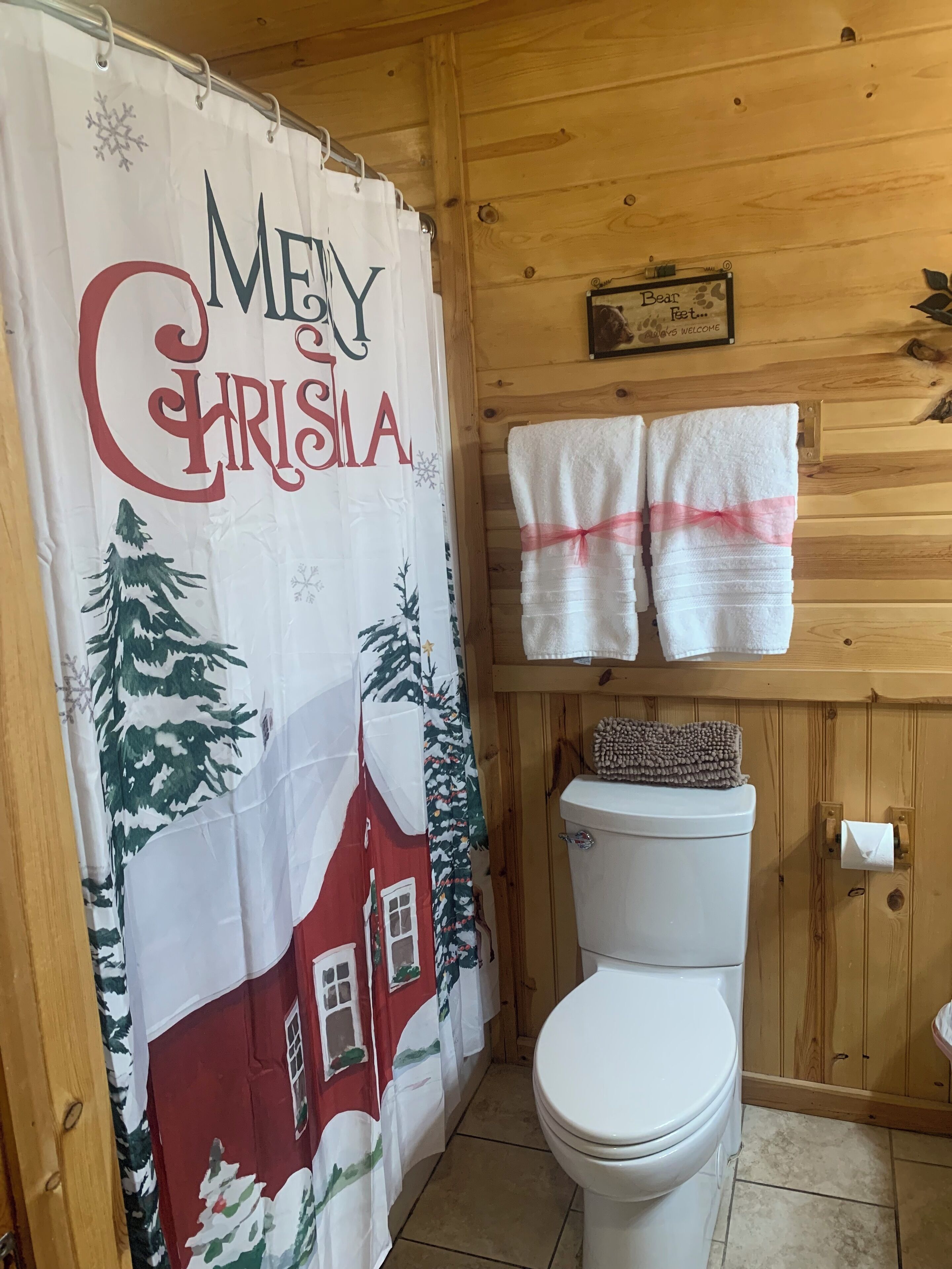 Une salle de bain avec des toilettes, un rideau de douche sur le thème de Noël et deux serviettes accrochées au mur.