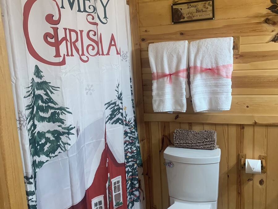 Une salle de bain avec des toilettes, un rideau de douche sur le thème de Noël et deux serviettes accrochées au mur.