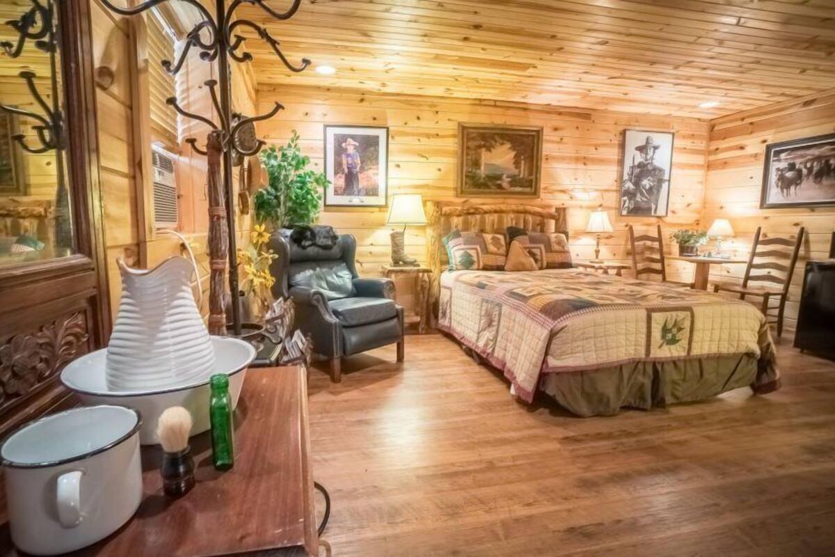 A cozy wooden cabin room with a bed, a chair, a table, and a lamp.