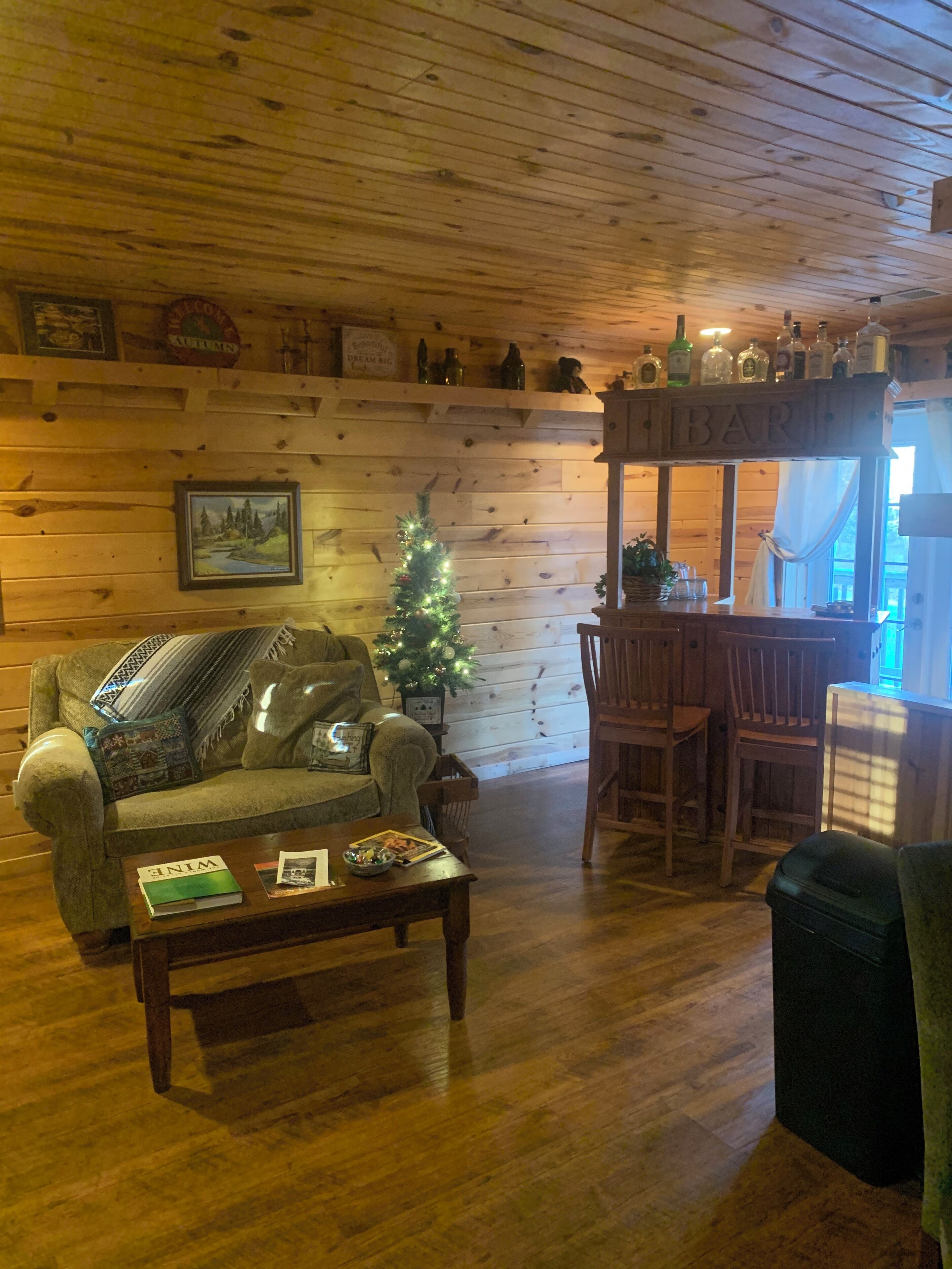 Interior acogedor de una cabaña con techo de madera, un árbol de Navidad, un sofá, una mesa de centro y una zona de bar.