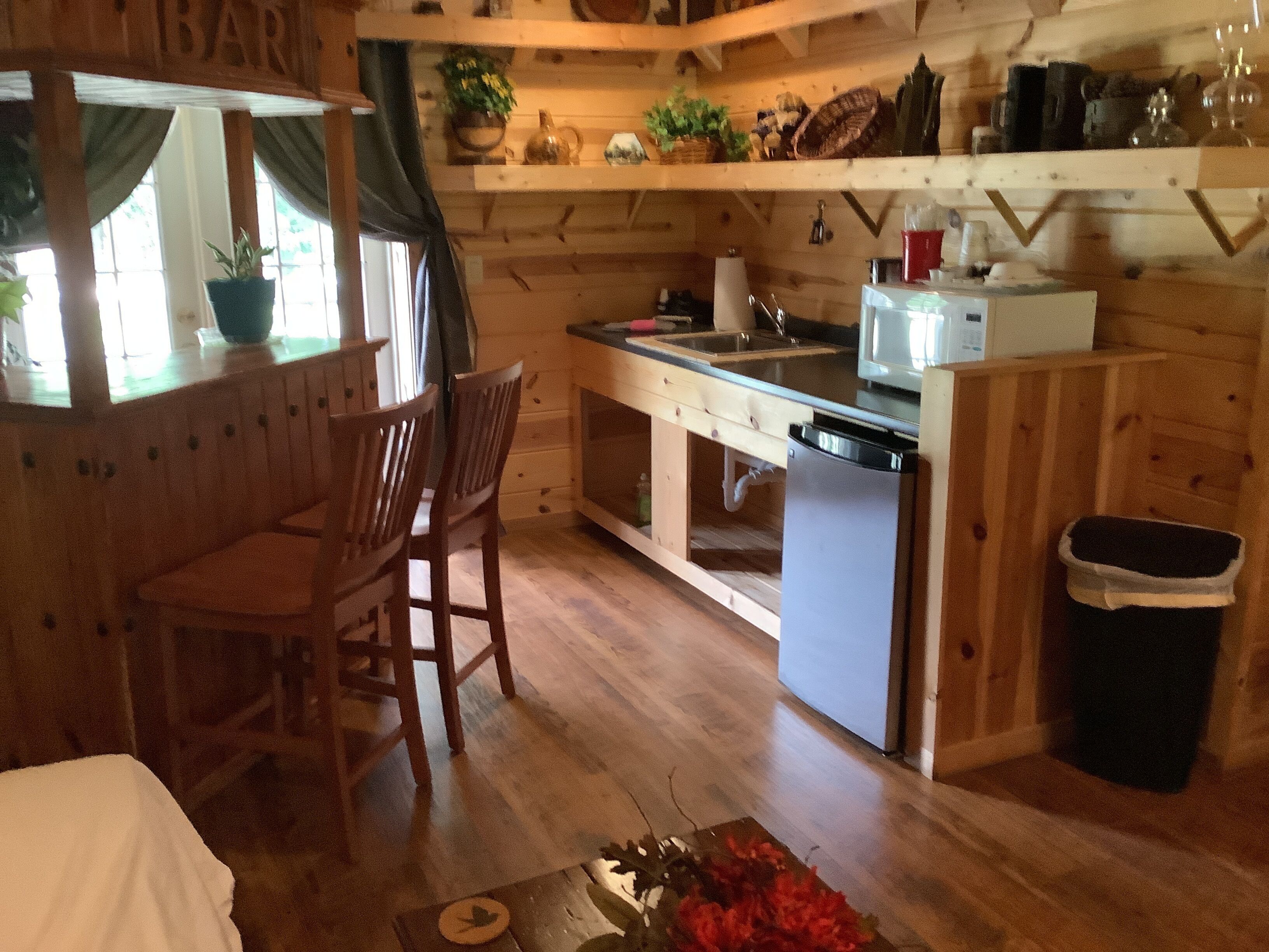 Un interior de madera con zona de cocina, sillas de madera, una pequeña mesa de comedor y un cubo de basura.