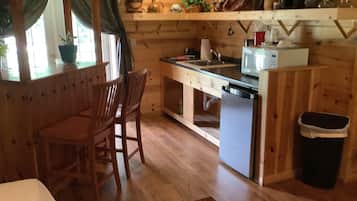 Un interior de madera con zona de cocina, sillas de madera, una pequeña mesa de comedor y un cubo de basura.