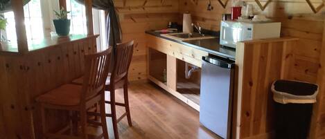 Een houten interieur met een keukenhoek, houten stoelen, een eettafeltje en een prullenbak.