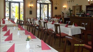 Een restaurant met meerdere tafels gedekt voor diners, met witte tafelkleden, rode servetten en vazen met bloemen.
