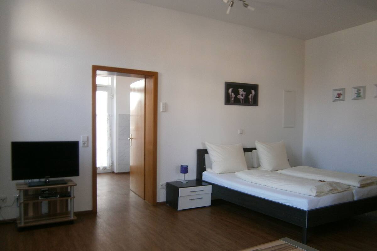 Een slaapkamer met een bed, een televisie, een nachtkastje en een deur naar een andere kamer.