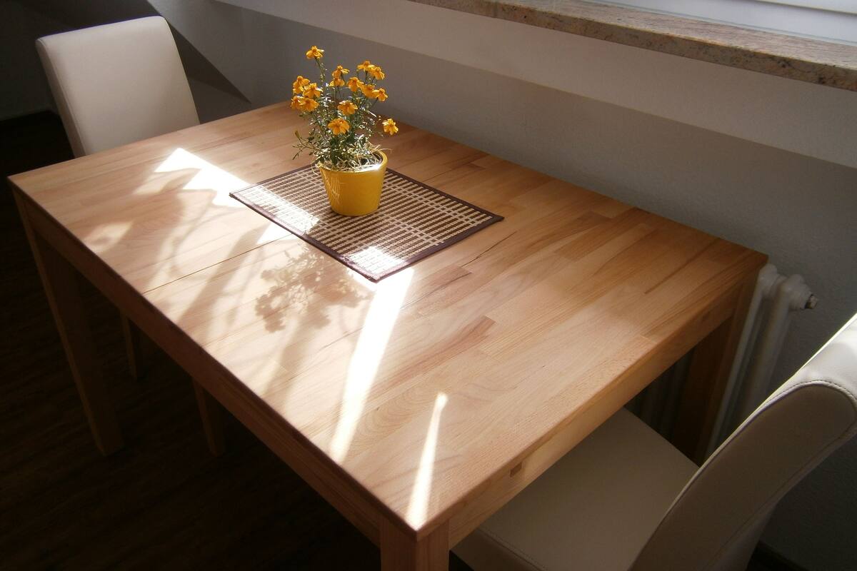 Een houten eettafel met een gele bloempot vol gele bloemen op een geweven tafelmat.