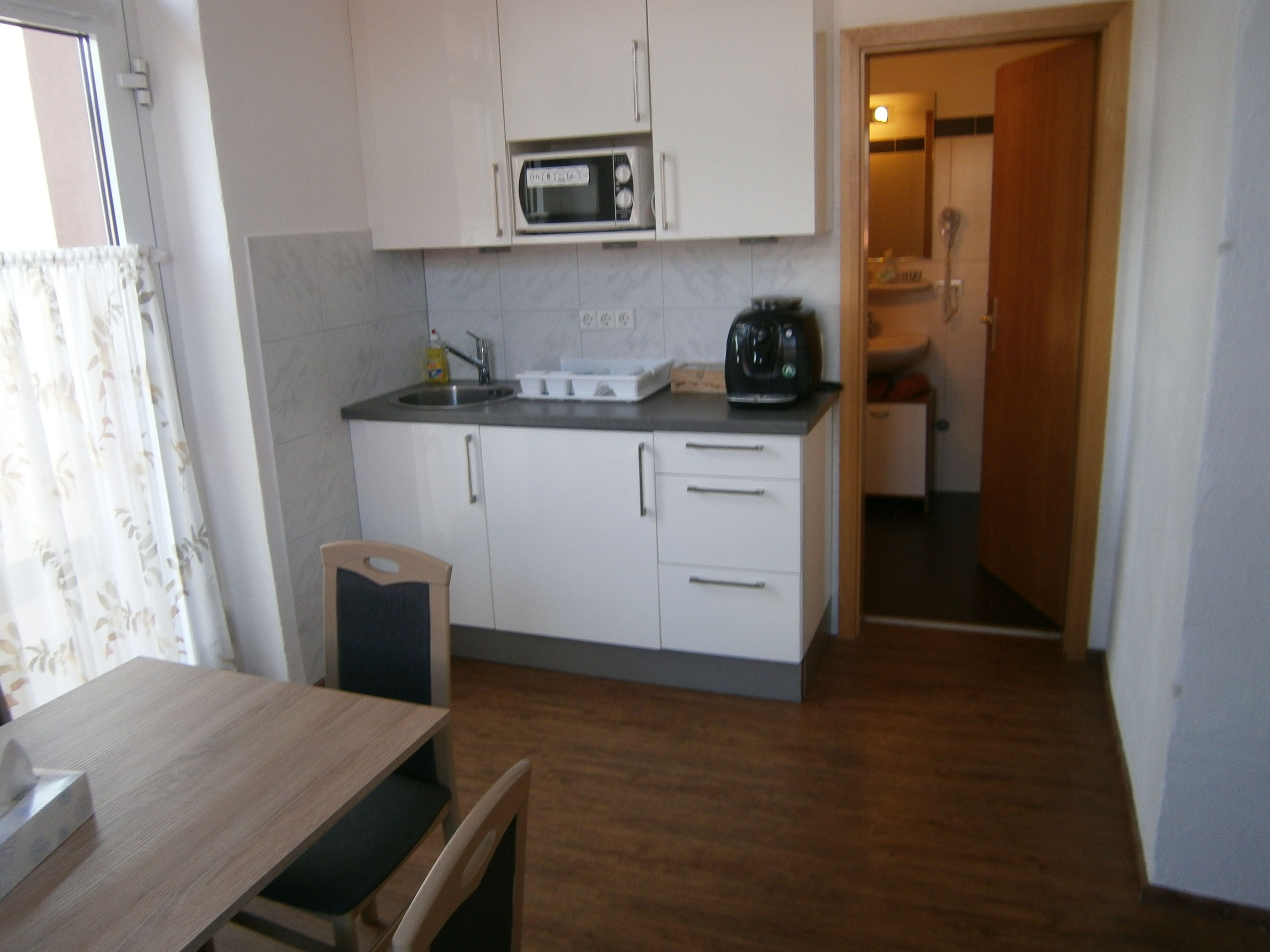 A compact kitchen with white cabinets, a microwave, a sink, and a coffee maker.