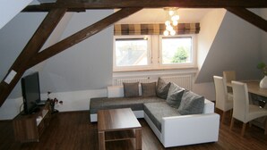 Een modern loft appartement met een houten plafond, een grijze modulaire bank, een witte salontafel en een eethoek met een witte tafel en stoelen.