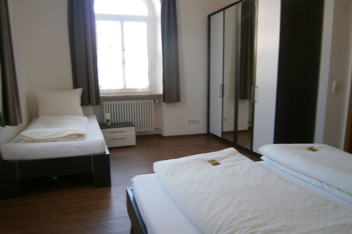 Een hotelkamer met twee eenpersoonsbedden, een klein nachtkastje, een radiator, een raam met gordijnen en een kledingkast.