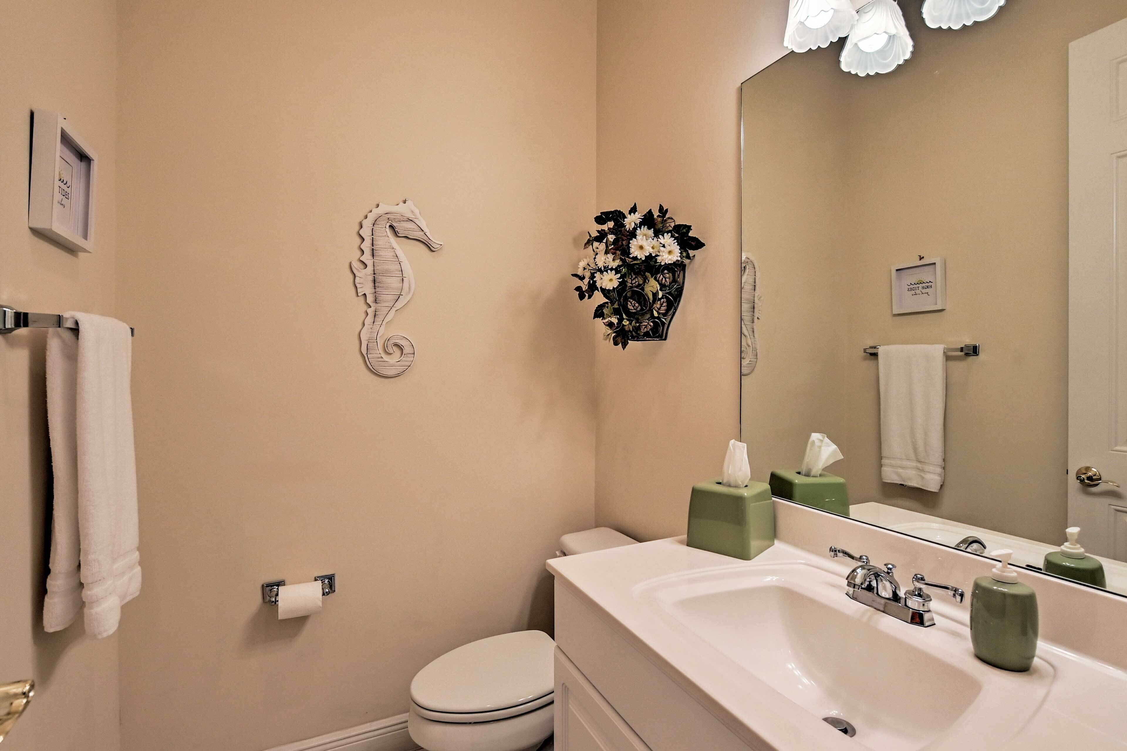 Een badkamer met toilet, wastafel en spiegel. Handdoeken hangen aan de muur en er staat een bloemenboeket.
