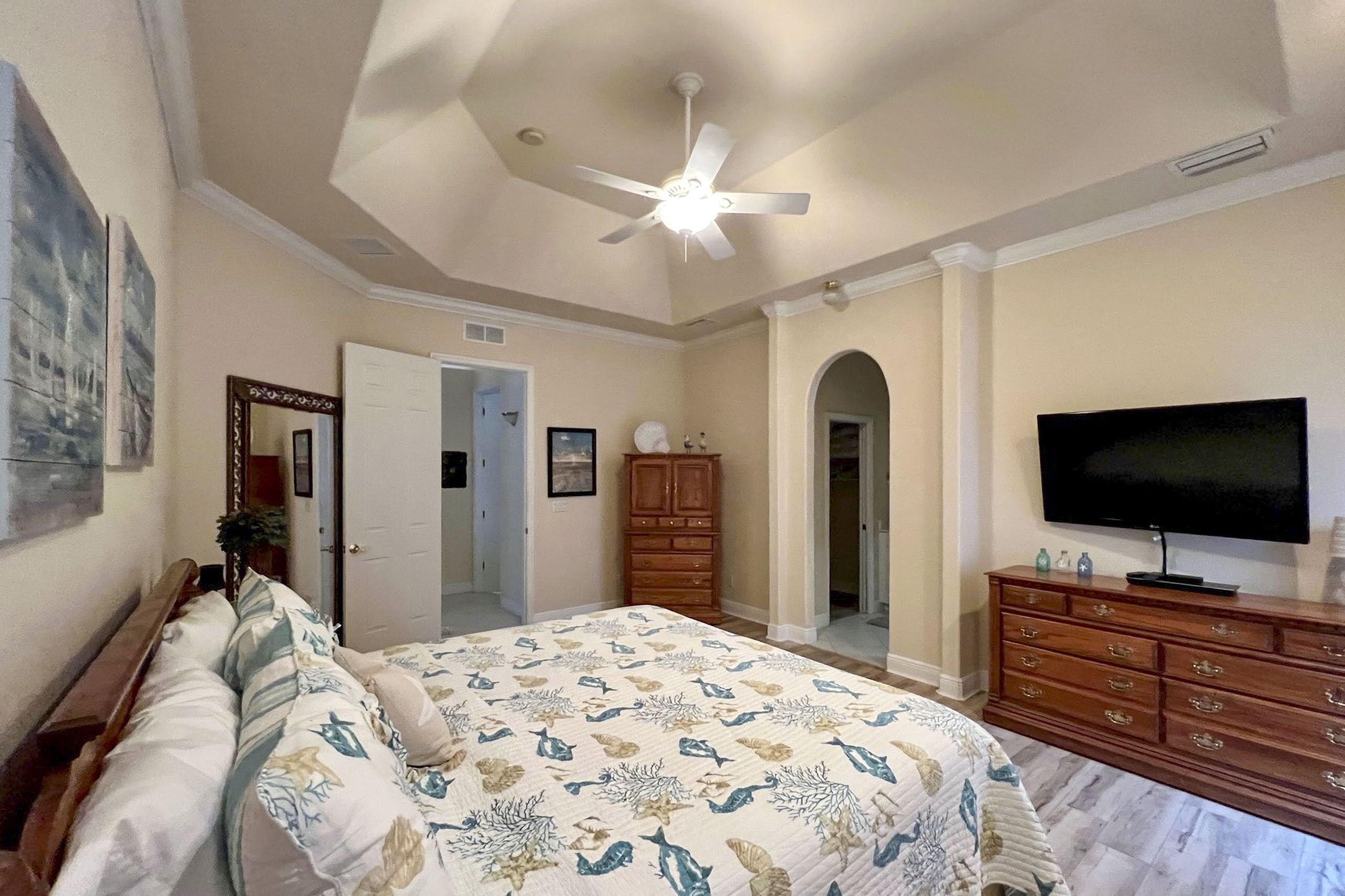 A bedroom with a bed, a ceiling fan, a TV, and a wooden dresser.