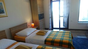 Ein Hotelzimmer mit zwei Betten, einem Nachttisch mit Lampe, einem Fenster mit Vorhängen und Blick ins Freie.