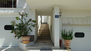Ein Gebäudeeingang mit einer Treppe, die zu einer Tür mit der Nummer 34 führt. An beiden Seiten des Eingangs befinden sich je ein Blumentopf.